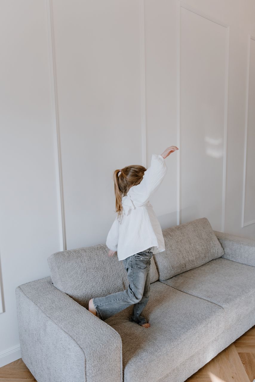 Kind tanzt mit erhobenem Arm auf einem Sofa